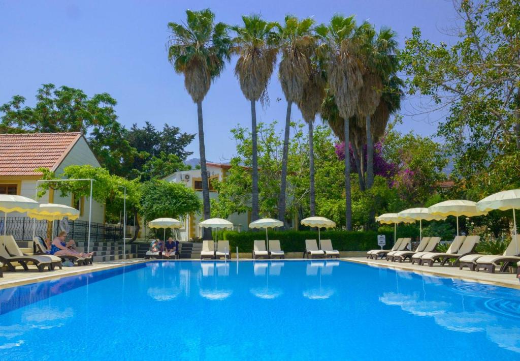 een zwembad met stoelen, parasols en palmbomen bij Riverside Garden Resort in Kyrenia