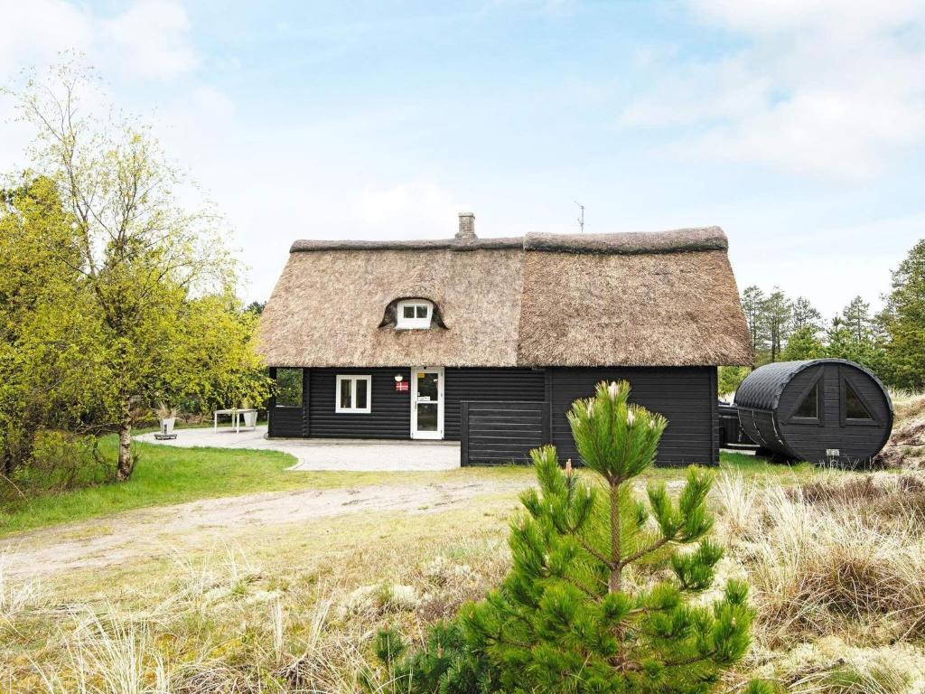 una casa negra con techo de paja y un árbol en 6 person holiday home in R m, en Vesterhede