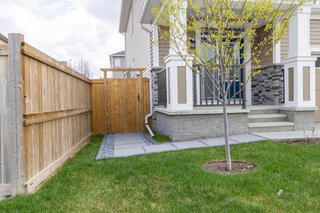 una valla de madera frente a una casa con un árbol en The Jade Place en Airdrie