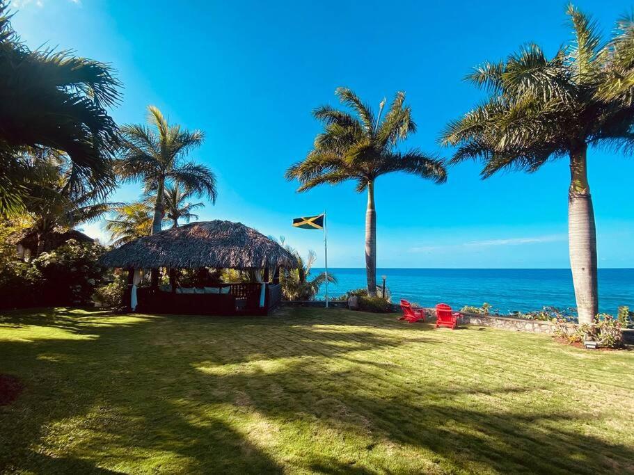 Oceanside Villa @ Ocho Rios, Jamaica Getaway في Boscobel: شرفة على الشاطئ مع أشجار النخيل والمحيط