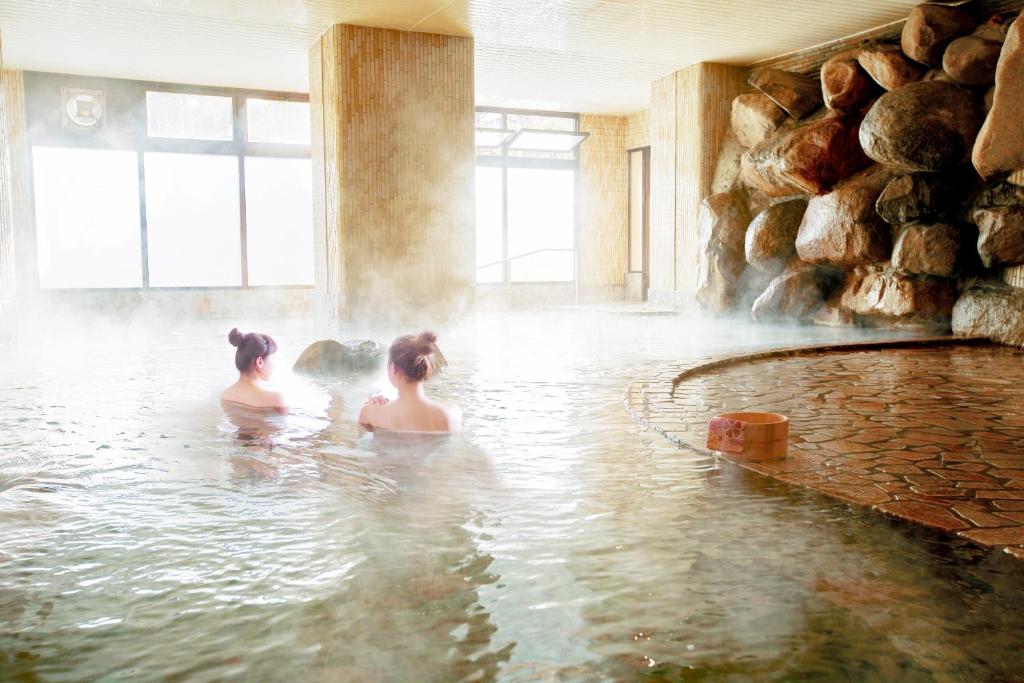duas mulheres sentadas na água numa banheira de hidromassagem em Ooedo Onsen Monogatari Hotel Shinko em Fuefuki