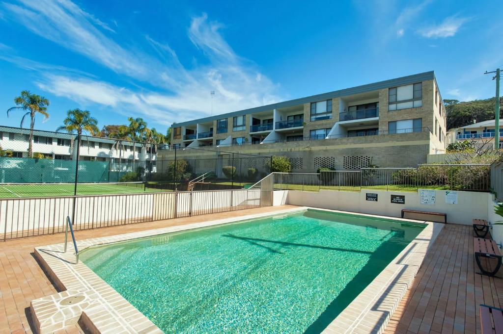 a swimming pool in front of a building at The Dunes Two bedroom apartment overlooking pool in Fingal Bay