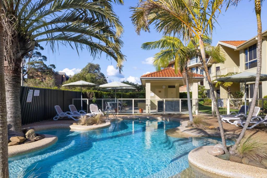 a pool with palm trees and chairs in a house at Martys Little Beach No 14 in Nelson Bay
