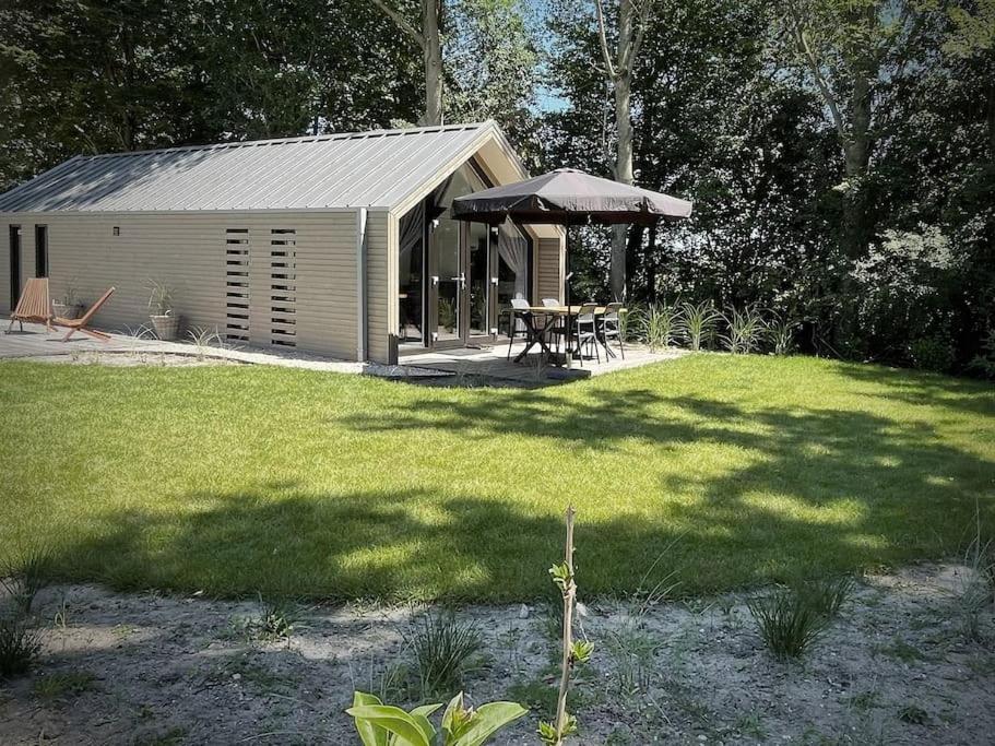 a shed with a table and an umbrella in a yard at Beachhouse Veluwemeer mit großem Garten in Strandnähe (inkl. Hallenbadnutzung) in Hulshorst