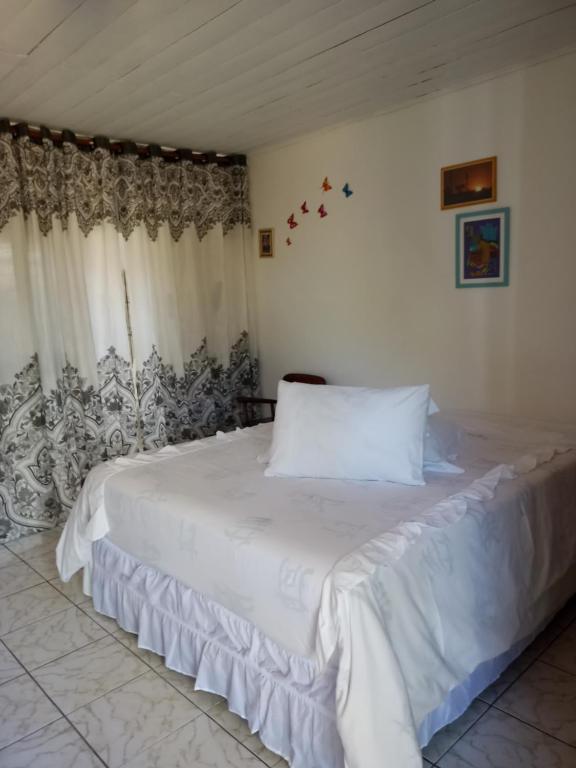 a bedroom with a large white bed with curtains at Suítes Novo Amanhecer in Sao Jorge