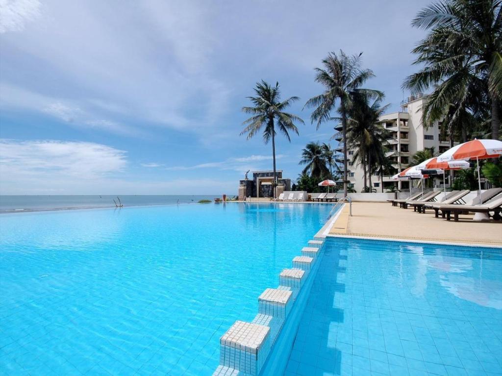 a large swimming pool next to a beach with palm trees at Golden Pine Beach Resort in Pran Buri