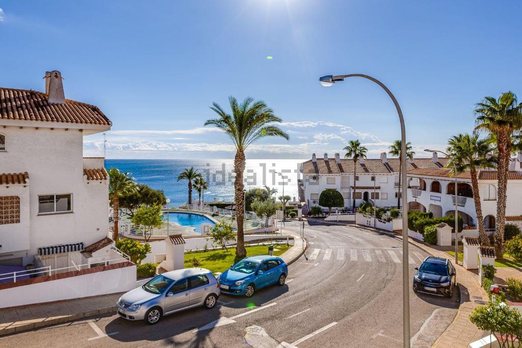 een straat met auto's geparkeerd voor gebouwen en de oceaan bij Aguamarina Playa in Orihuela