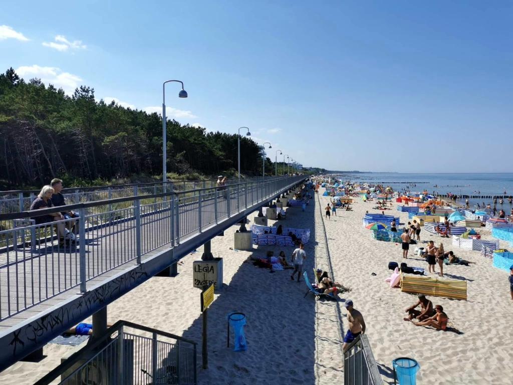 a beach with people sitting on the sand and a bridge at Pod Sosną in Mielno