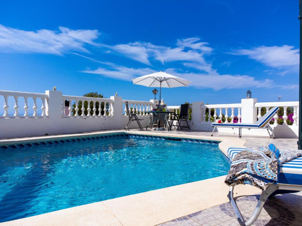 a swimming pool with chairs and a table and an umbrella at Villa Las Brisas by Interhome in Nerja