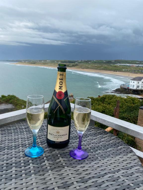 a bottle of wine and two glasses on a table with the ocean at Golden Sands in Portrush