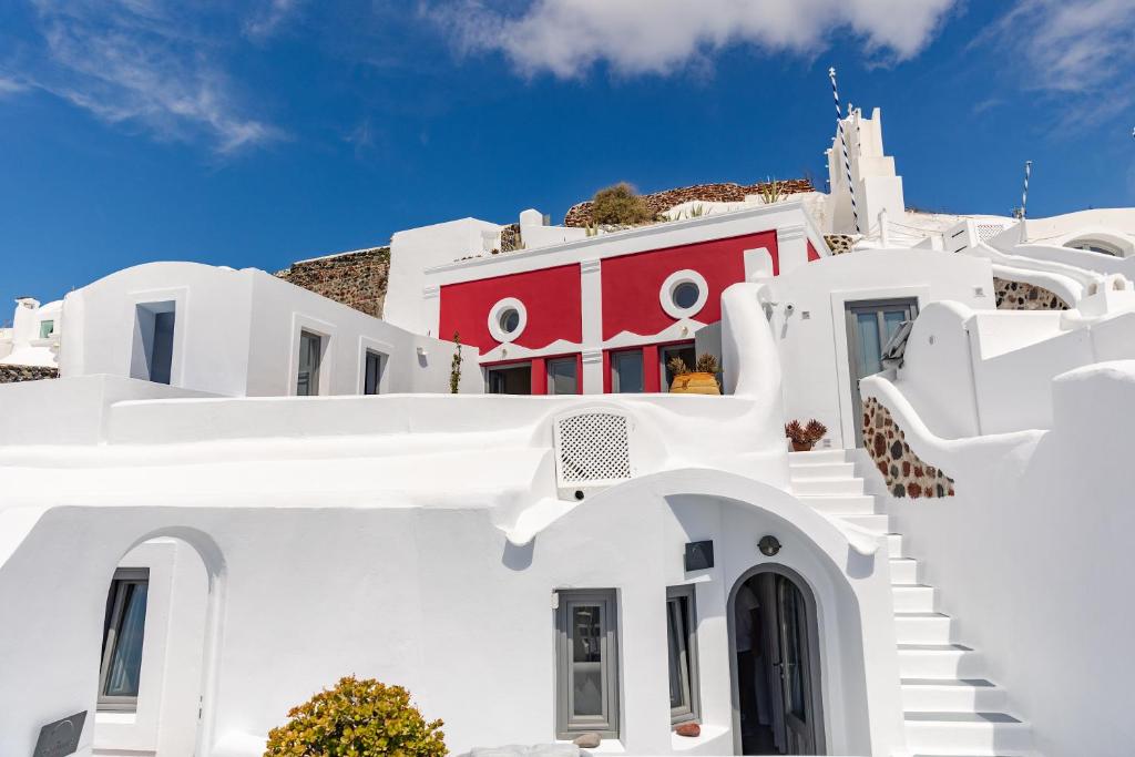 a white house with a red door and stairs at IKIES Santorini in Oia