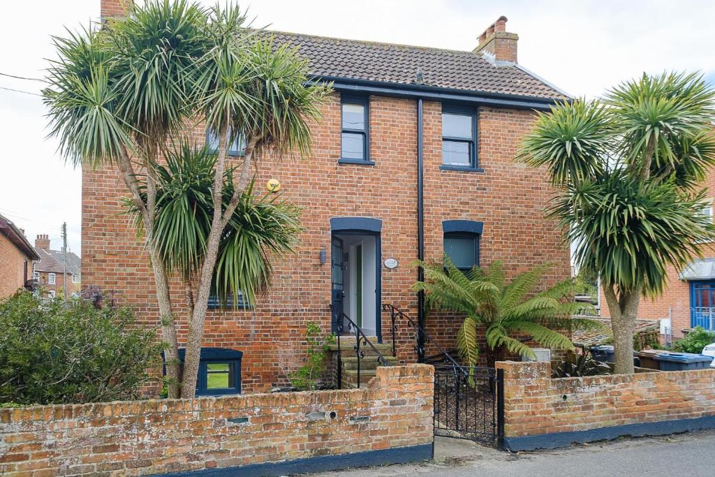 a brick house with palm trees in front of it at Frogmore Cottage in Leiston