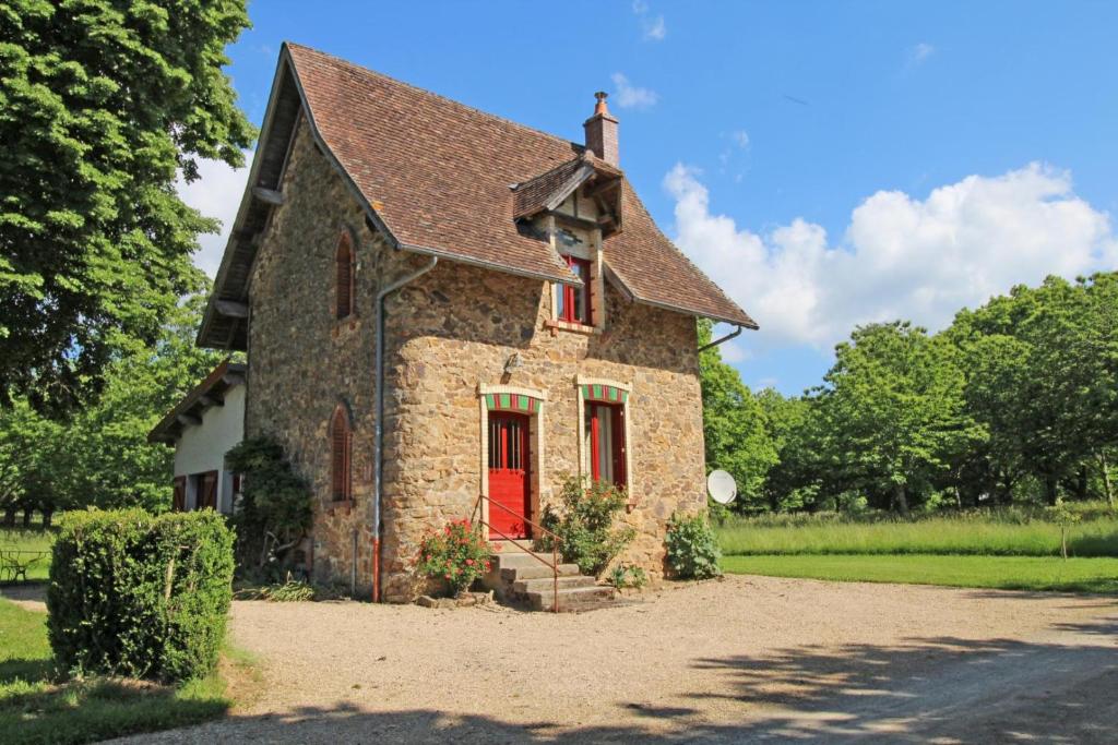uma pequena casa de pedra com uma porta vermelha em Les grangettes em Rilhac-Rancon