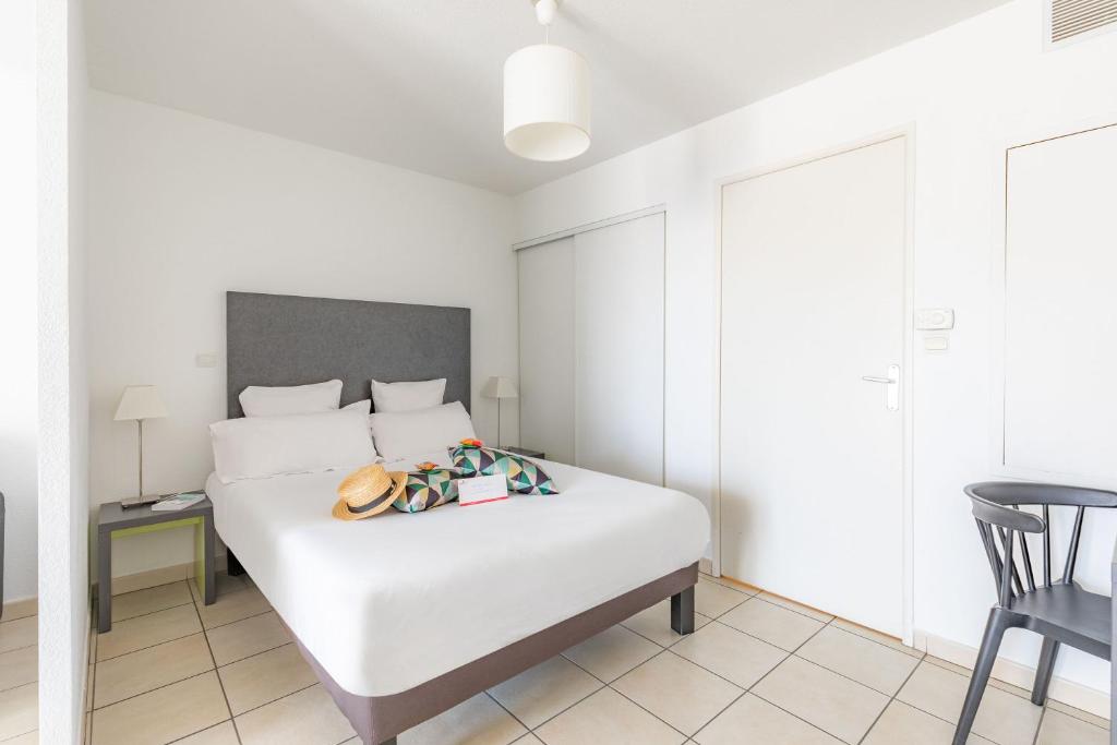 a bedroom with a white bed and a table and a chair at Appart'City Confort La Ciotat - Côté Port in La Ciotat