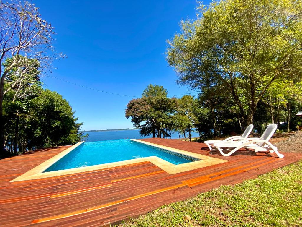 una piscina con 2 sillas blancas junto a una terraza de madera en Blusky Lodge en Puerto Iguazú