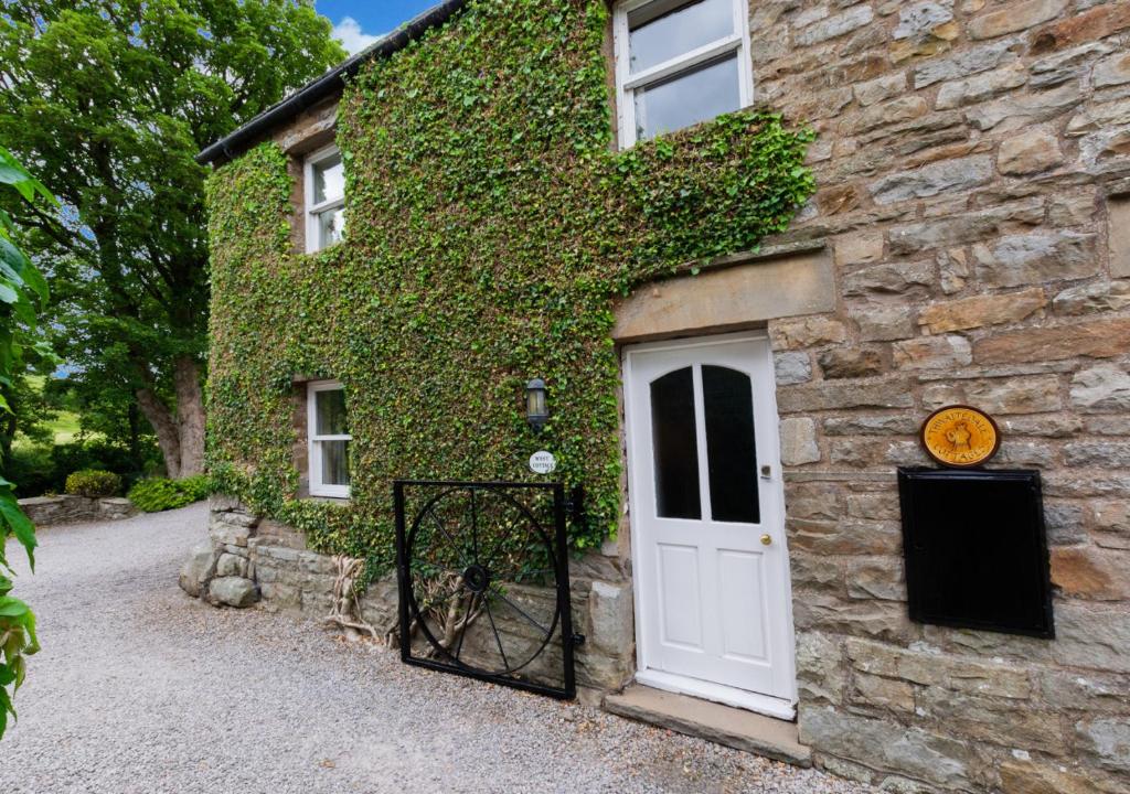 a stone house with a white door and ivy at West Cottage in Thwaite