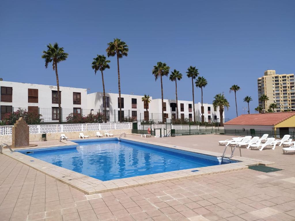 a large swimming pool with chairs and palm trees at Apartment Soleil Altamar in Playa de las Americas