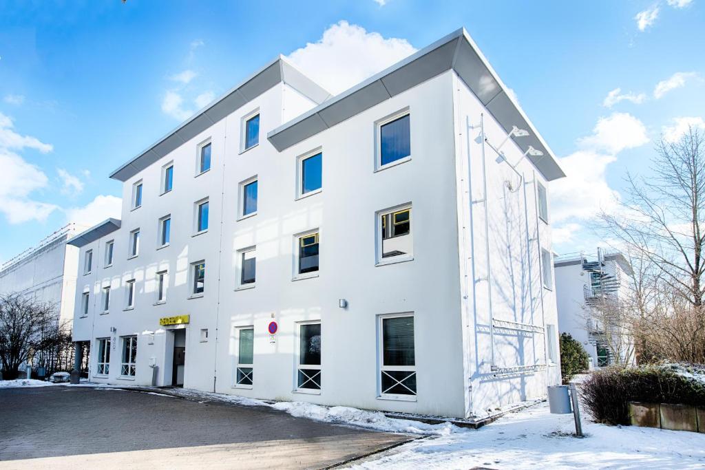 a white building with snow on the ground at B&B Hotel München-Putzbrunn in Putzbrunn