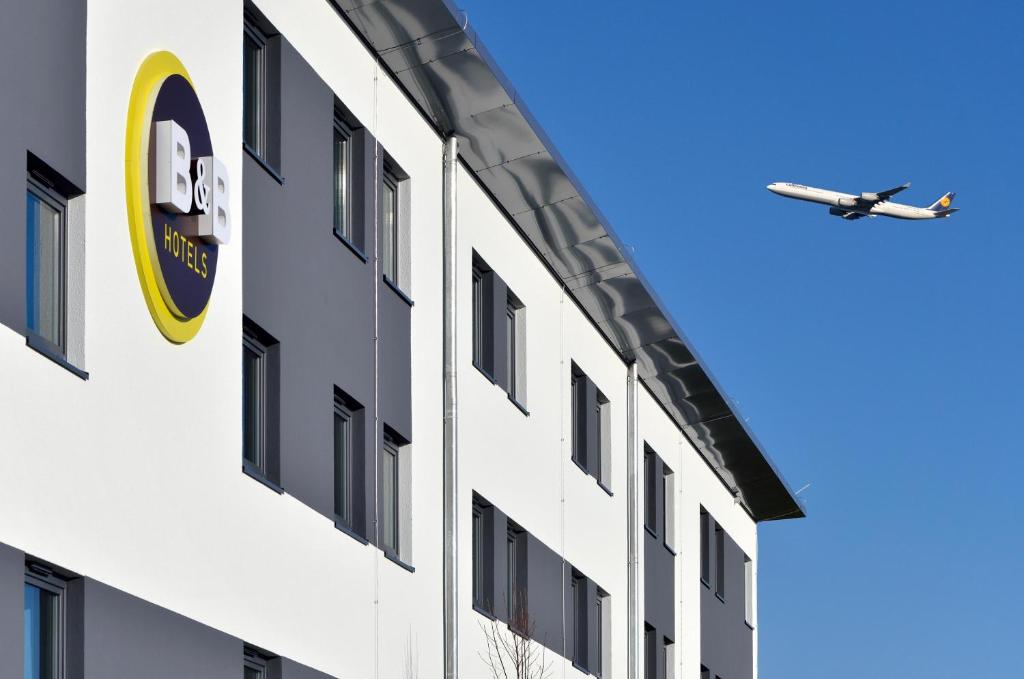 un avión sobrevolando un edificio con un hospital en B&B HOTEL München-Airport, en Hallbergmoos