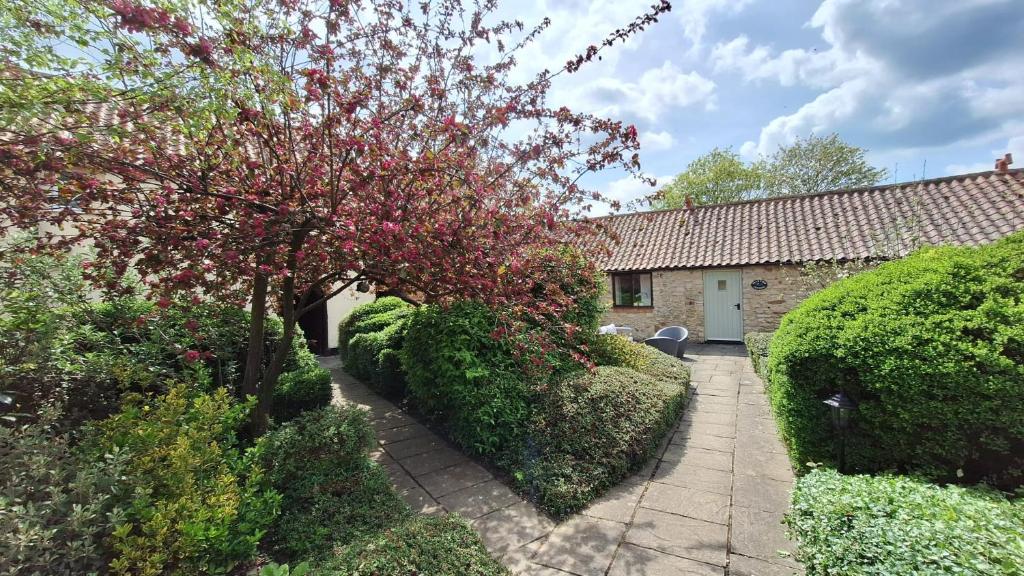 a house with bushes and a tree with red flowers at Osprey Meadow Holiday Cottages in Bedale