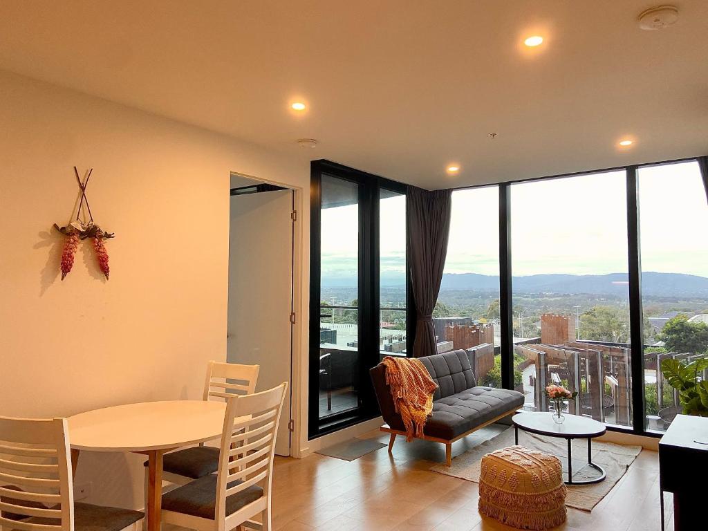 una sala de estar con mesa y sillas y una habitación con ventanas en Skygarden On The Glen, en Glen Waverley