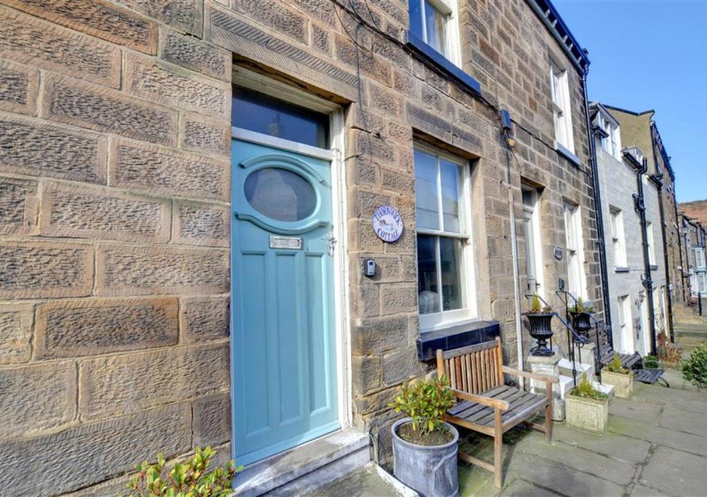 a blue door on a brick building with a bench at Thornwick Cottage in Staithes