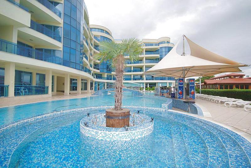 une grande piscine avec un palmier et un parasol dans l'établissement Marina Hotel Apartaments, à Pomorie