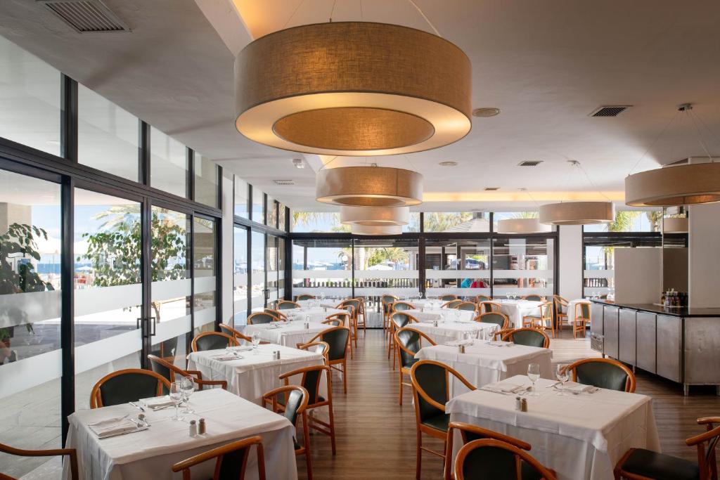 a restaurant with white tables and chairs and windows at Alexandre Grand Teguise Playa in Costa Teguise