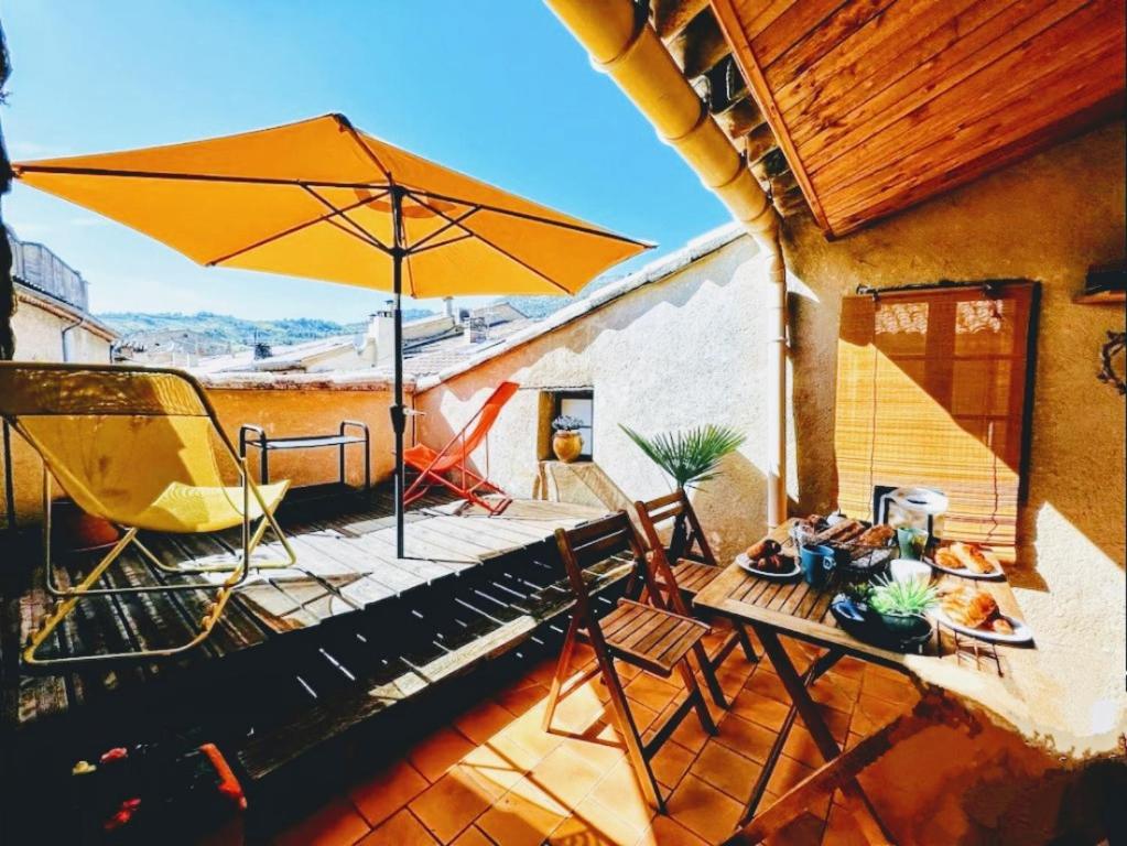eine Terrasse mit einem Tisch, einem Sonnenschirm und Stühlen in der Unterkunft La Terrasse d'Oléa, au coeur du village in Buis-les-Baronnies