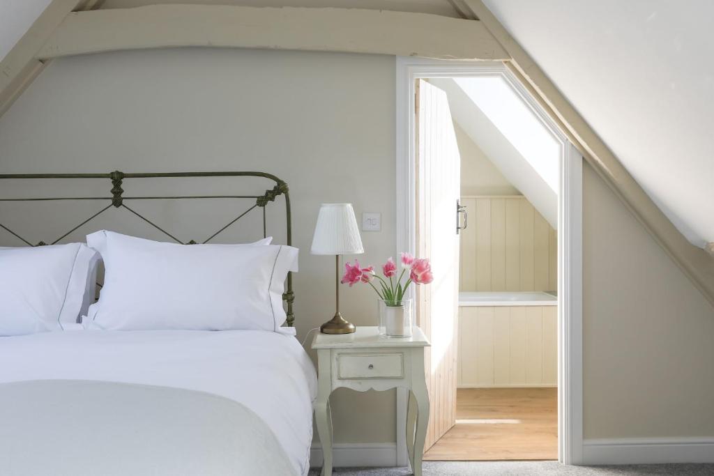 a bedroom with a white bed and a table with flowers at Coombers Mead Cottage in Tetbury