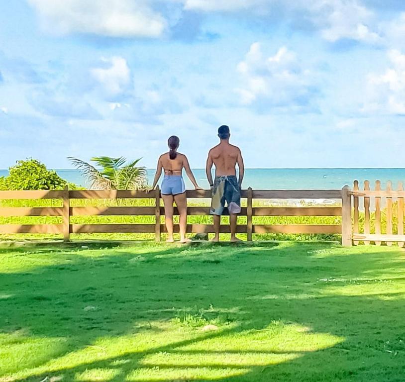 a man and woman standing on a fence looking at the ocean at casa de praia a beira mar in Campina