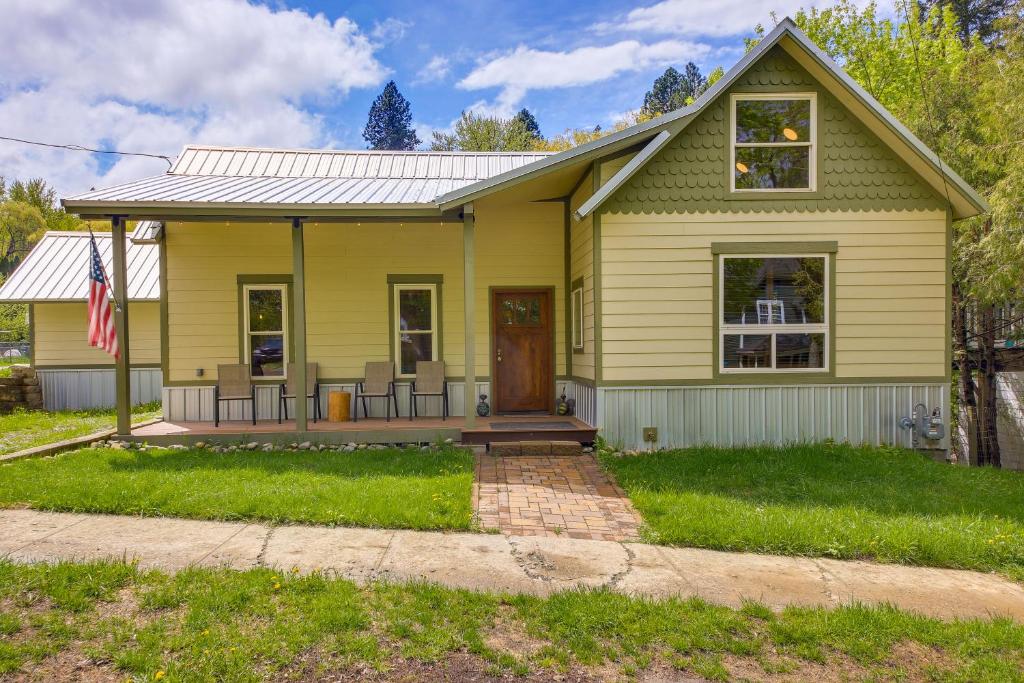 a yellow house with a flag in front of it at Downtown Bonners Ferry Home with Covered Porch! in Bonners Ferry