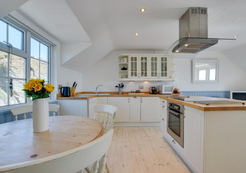 cocina con armarios blancos y mesa de madera en Cliff Top Cottage en Porthleven