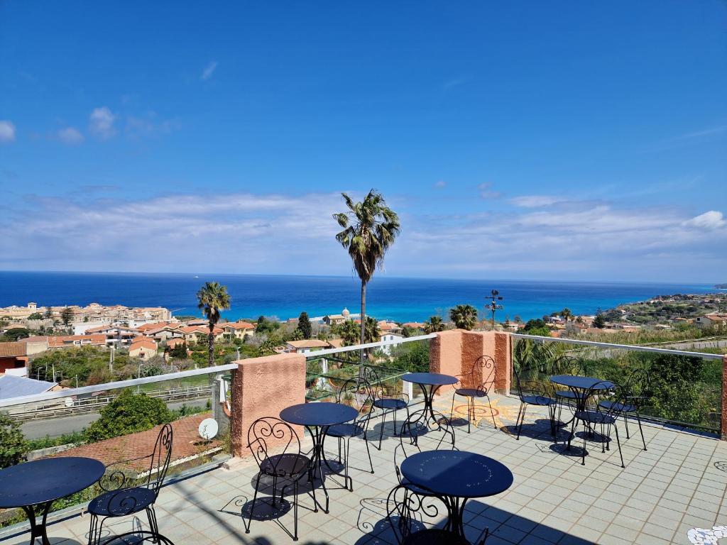 un patio con tavoli, sedie e vista sull'oceano di Hotel - Giardino Marchese D'Altavilla a Tropea