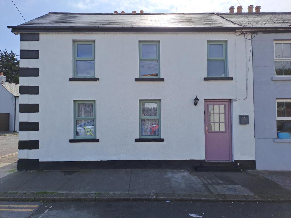 une maison blanche avec une porte et des fenêtres roses dans l'établissement 3 bed corner terrace house by the sea Wicklow town, à Wicklow