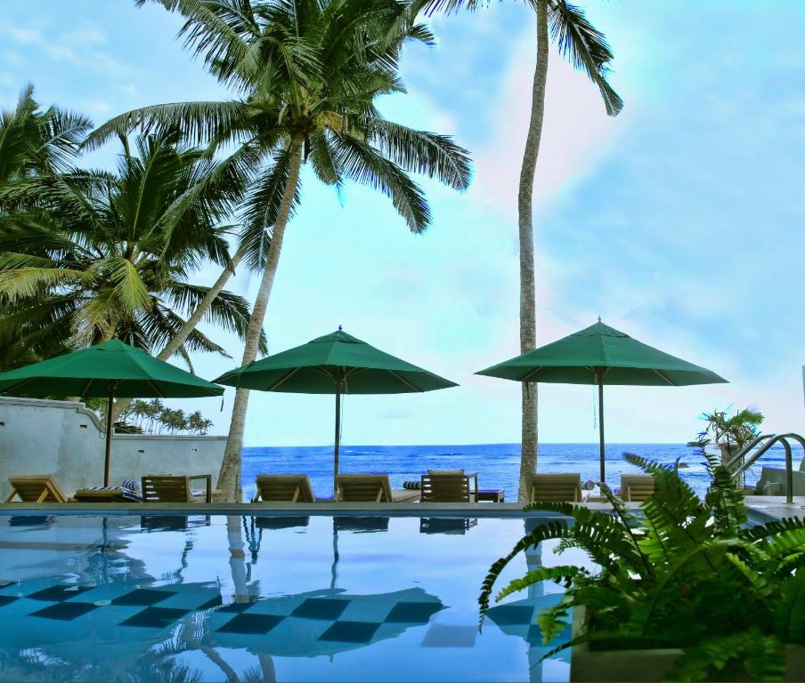 a swimming pool with umbrellas and the ocean at Sea World Boutique Hotel in Mirissa