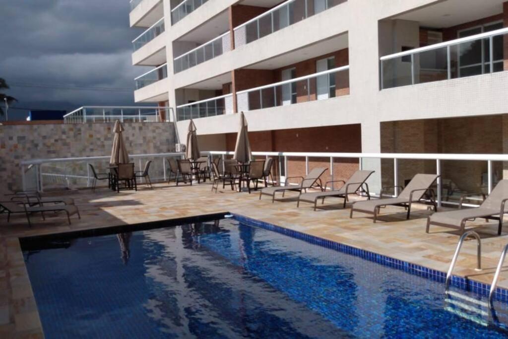 a hotel with a swimming pool and chairs and a building at Apto. com varanda gourmet e piscina aquecida in Bertioga