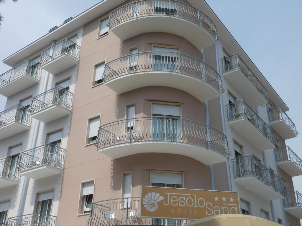 un edificio con balconi e un cartello di fronte ad esso di Hotel Jesolo Sand a Lido di Jesolo