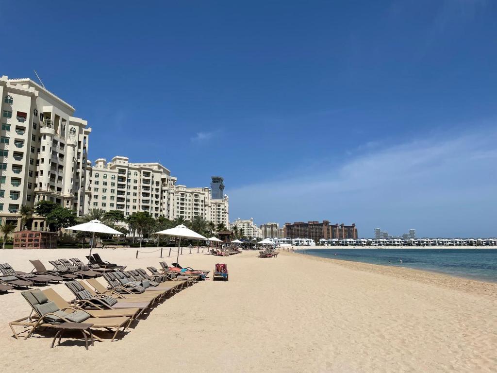 a beach with chairs and umbrellas and the ocean at Al Dabas Beach Views, 3BD Sleeps 6, Beachfront Beach & Pool Access in Dubai