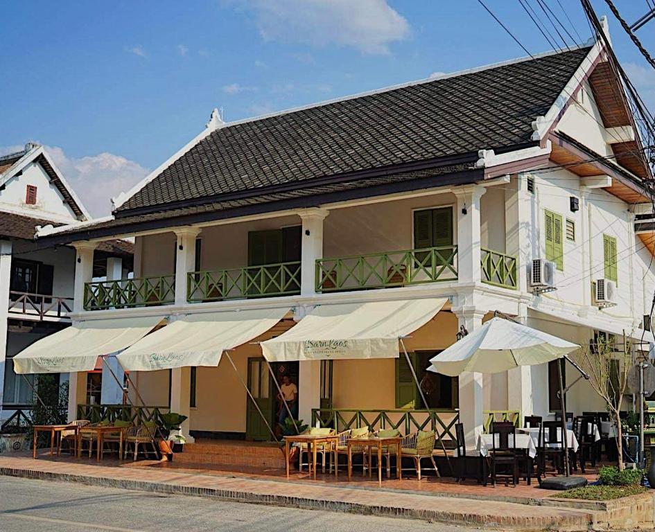 a building with tables and umbrellas in front of it at Barn Laos Luangprabang Hostel in Luang Prabang