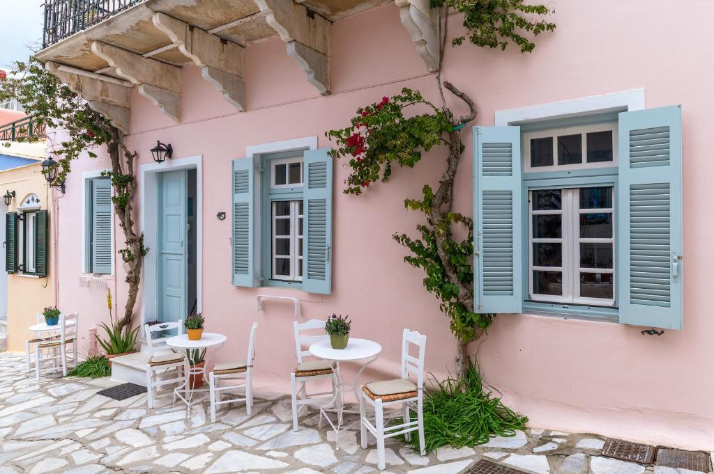 a pink house with blue windows and tables and chairs at Apano Vrysi Tinos 3 in Tinos