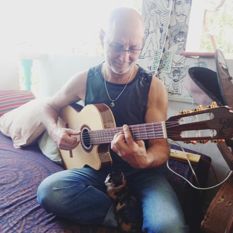 a man sitting on a bed playing a guitar with a cat at Dreamcatcher House & Hostel at Arambol Beach in Arambol