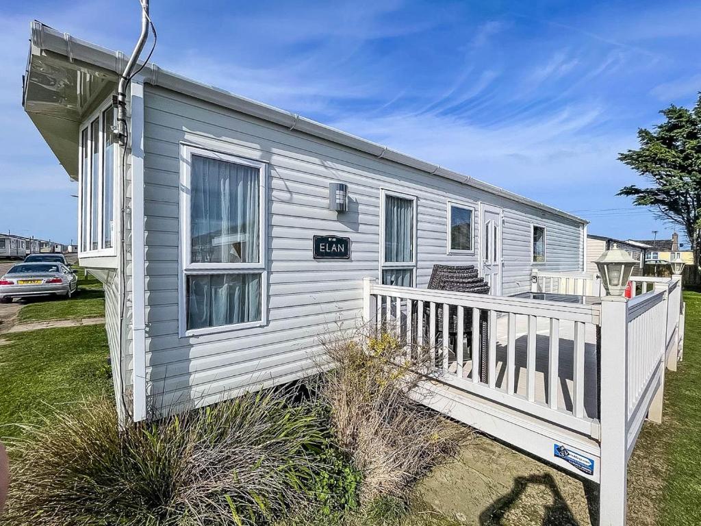 a white tiny house with a porch and a fence at Lovely Caravan With Decking Nearby Scratby Beach In Norfolk Ref 50031j in Great Yarmouth