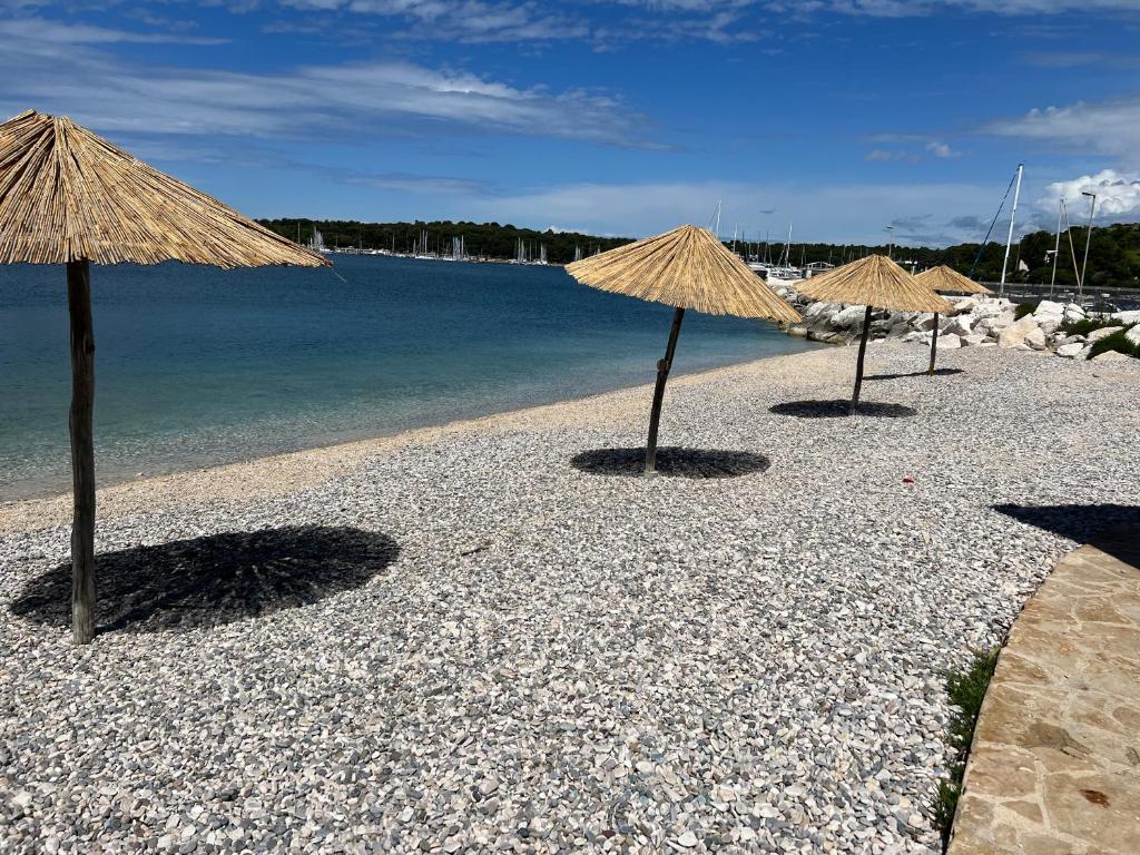 three straw umbrellas on a beach near the water at Apartments By The Sea in Pula
