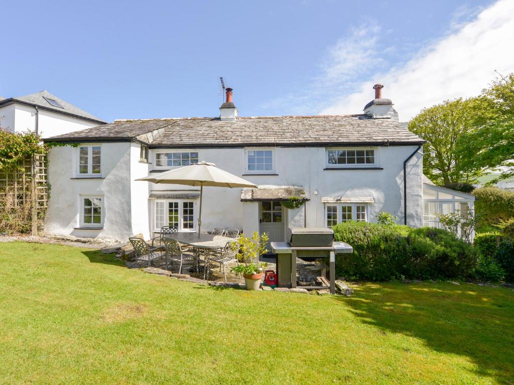 Casa blanca con mesa y sombrilla en Ayr Cottage, en Tintagel
