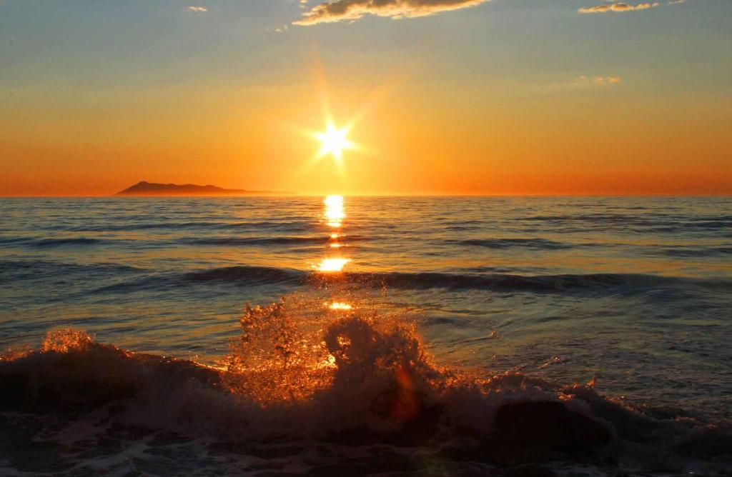 Une vague dans l'océan avec le soleil dans le ciel dans l'établissement Logas Beach Studios Peroulades Corfu, à Peroulades