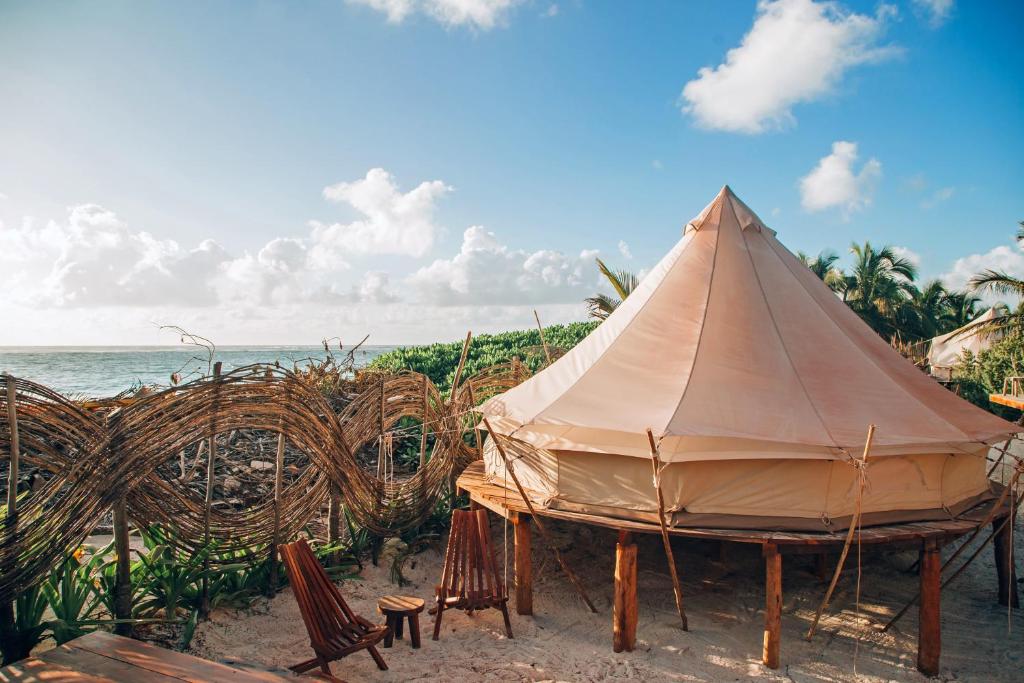 a tent on the beach with chairs and the ocean at GlampIKAL formerly Casa Nawal in Tulum