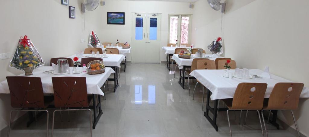 una sala da pranzo con tavoli e sedie bianchi e una stanza con pareti bianche di GUINDY CHENNAI STAYS a Chennai