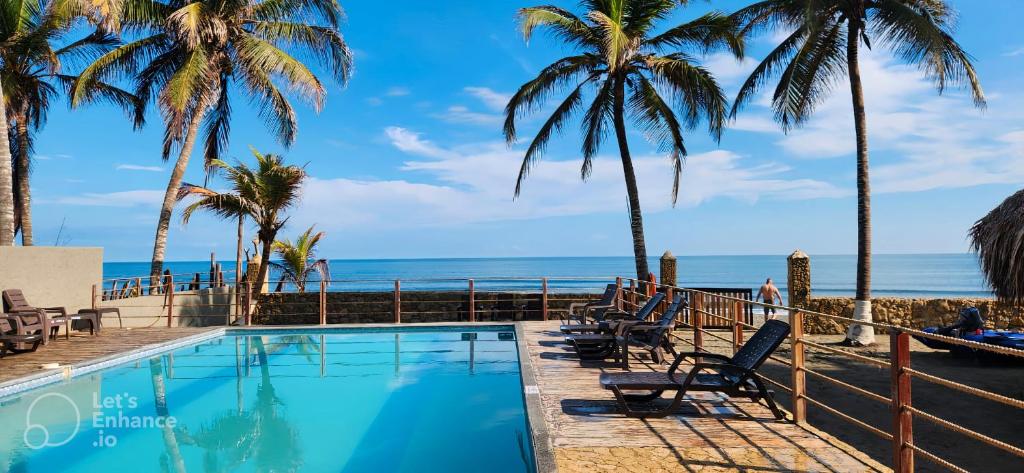 una piscina con palmeras y el océano en Sereni San Bernardo Hotel Playa en San Bernardo del Viento
