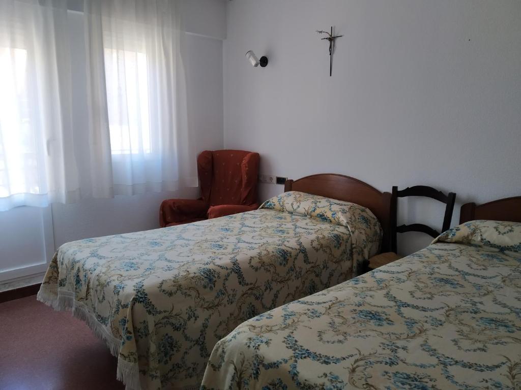 um quarto de hotel com duas camas e uma cadeira em Albergue La Esperanza de la Sagrada Familia em Melgar de Fernamental